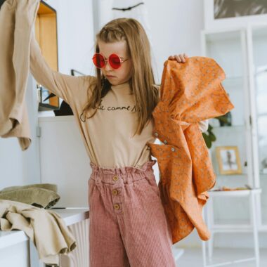 Fashionable young girl wearing stylish outfit and sunglasses in modern boutique, showcasing clothing selection.